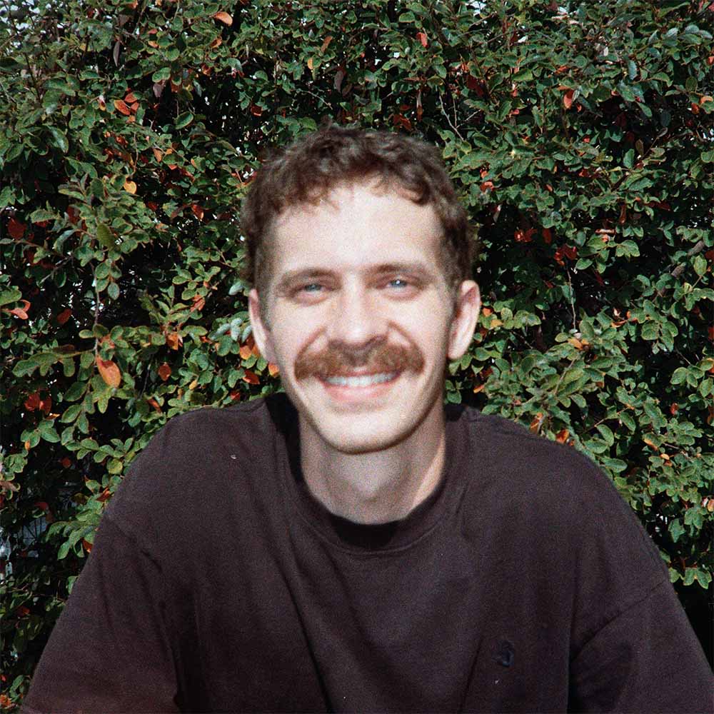 Trent Teinert smiling in front of green foliage